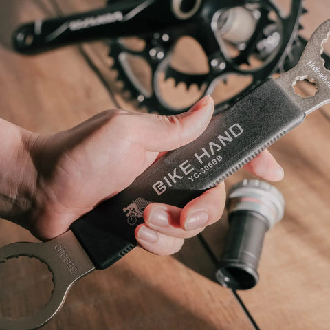 Close-up of a hand holding a 16 notch bottom bracket tool, engraved with 'BIKE HAND YC-306BB', on a wooden surface.