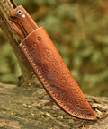 Full Tang Hunting Knife With 10 Inch Overall Length, 5 Inch High Carbon Steel Blade, Rosewood Handle, And Sheath displayed on wood