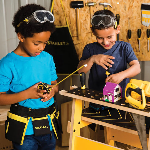 Two kids using Real Deal Kids Tool Set With Belt Pouch, 10 Piece Pretend Play Tools in a woodworking setting with goggles on.