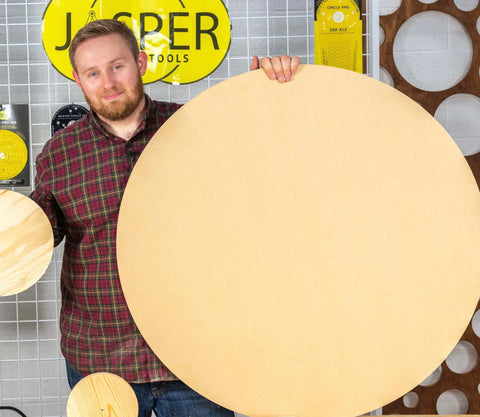 Man holding large wooden disc made with Blemish Free Pivot Plate For Circle Cutting No Center Hole Required For Flawless Discs And Tabletops Clean Edges Easy Router Jig Accessory Works With All Circle Cut Guides For Top Notch Results, standing in workshop with Jasper Tools background.