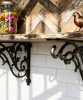 16 Inch Cast Iron Shelf Brackets 4 Pack Black Corbels mounted under a rustic shelf with decorative jars and a bird figurine.