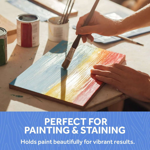 Baltic birch plywood craft board being painted with blue, yellow, and red strokes; paint cans and brushes visible.