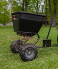Tow Behind Broadcast Spreader With Universal Hitch 175 Lb Capacity Durable Poly Hopper spreading seed on lawn