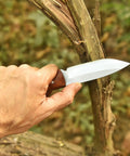 Full Tang Hunting Knife With 10 Inch Overall Length held in hand with hardwood, cutting through a branch outdoors.