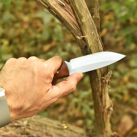 Full Tang Hunting Knife With 10 Inch Overall Length held in hand with hardwood, cutting through a branch outdoors.