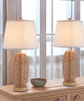 Two wicker table lamps with white shades on a wooden console in a bright room, modern decor setup.