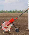Person using Six Nozzle Walk Behind Seed Spreader For Precise Row Crop Planting Hand Push Seeder for soybeans in field.