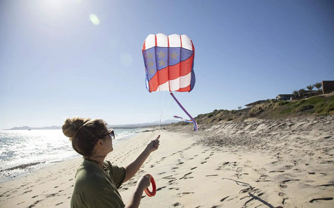 Person flying Patriot Wave 7.5 Parafoil Kite, Easy To Fly Single Line Beginner Kite With No Assembly, on a sandy beach.