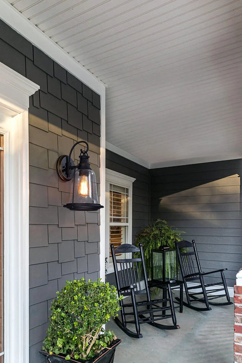 Brynn One Light Outdoor Wall Light with oil rubbed bronze finish and clear seeded glass on porch near rocking chairs.