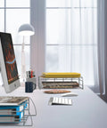 Modern office desk with computer monitor, desk lamp, and stackable metal file organizers holding paper and files.
