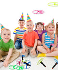 Kids playing with Awesome Flying Saucer Toy Set With 32 Discs And 16 String Launchers, wearing party hats indoors.