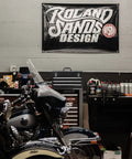 Motorcycle parked in garage with tool storage and banner labeled 'Roland Sands Design' on the wall.