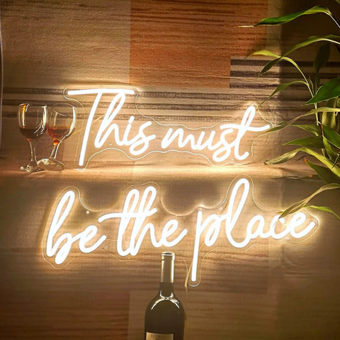 Large 43.7x8 Inch Neon Sign LED Wall Decor for Wedding Bar Office Cafe Party, reads 'This must be the place', with plants and glasses