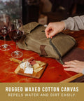 Straight Up Insulated Wine Bag With Matching Cheese Board And Sharp Corkscrew Opener Waxed Canvas Cooler Tote For Two Bottles Pocketed Grab And Go Hauler For Weekend Kickbacks In Khaki Green with cheese board and wine glasses.