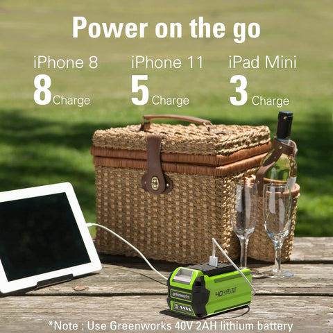 Picnic basket with electronics charging from Greenworks 40V inverter, next to wine glasses and a tablet, illustrating portable power.