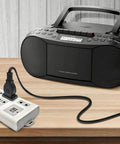 Black radio cassette player connected to a white power strip with multiple outlets on a wooden table.