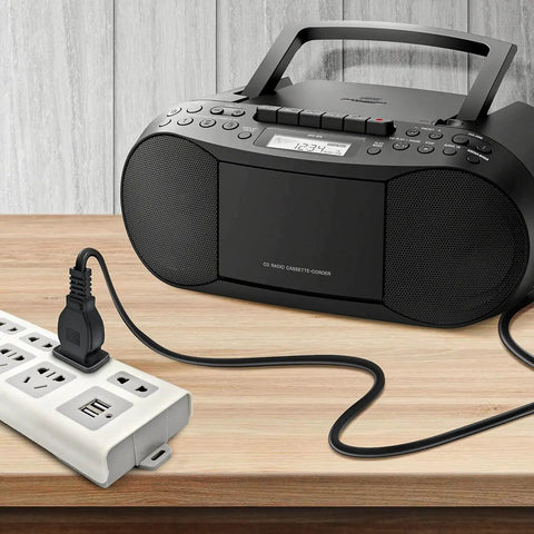 Black radio cassette player connected to a white power strip with multiple outlets on a wooden table.