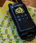 Close-up of a walkie-talkie placed on yellow $5 and $10 price stickers from Yard Sale EZ Kit Neon Yellow Signs 11 By 14 Inches With 600 Prepriced Stickers Price Label Sheets And Arrows For Directing Customers Includes 15 Writable Large Stickers And Repriced Sticker Pack For Fast Pricing.