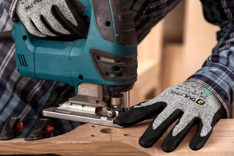 Person using a jigsaw while wearing A3 Cut Resistant Work Gloves For Men And Women Foam Nitrile Coated With Touchscreen Friendly Tips 12 Pairs ANSI A3 Rating Pro Grade Heavy Duty Grip For Glass Cutting And Automotive Shop Tasks.