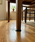 Twenty Pack Rubber Leveling Shims Anti Wobble Furniture Levelers under a wooden table leg on hardwood floor.