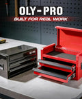 Mini Toolbox With Two Drawers And Top Storage In Durable Steel Smooth Glide Ball Bearing Slides Portable Tool Box Organizer For Garage Workshop School Or Office Use In Red with open drawers next to closed black toolbox on workbench.