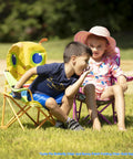 Children sitting on Giddy Buggy Kid-Sized Folding Lawn And Camping Chair With Cup Holder, water-resistant fabric in a grassy area.