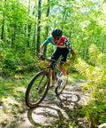 Mountain biker riding through a forest trail, showcasing Endurance Formula Tubeless Bike Tire Sealant With Injector For MTB Road CX And Gravel Bikes Eight Ounce Bottle Long Lasting Fast Sealing With Nanoparticle Technology Seals Punctures Up To One Quarter Inch effectiveness during a ride.
