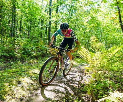 Mountain biker riding through a forest trail, showcasing Endurance Formula Tubeless Bike Tire Sealant With Injector For MTB Road CX And Gravel Bikes Eight Ounce Bottle Long Lasting Fast Sealing With Nanoparticle Technology Seals Punctures Up To One Quarter Inch effectiveness during a ride.