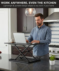 Man using 32 By 22 Inch Standing Desk Converter With Gas Spring Lift Slim Two And A Half Inch Low Profile Sit Stand Desk Riser in kitchen