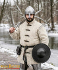 Warrior holding sword and Beefy Battle Ready 11 Inch Small Medieval Buckler Shield With Rolled Rim And Riveted Grip 16 Gauge Mild Steel For LARP Reenactment Stage Use And Display Blackened Compact Round Shield in snowy forest