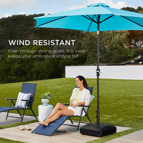 123 Pound Fillable Mobile Umbrella Base With Four Wheels Two Locks And Two Tightening Knobs For Patio Deck Or Poolside Wind Resistant Design Beefy Heavy Duty Weatherproof Reservoir For Easy Refill And Stable Position Black supporting an open blue umbrella on a patio with seating and greenery in background.