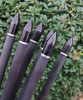Five black carbon crossbow bolts with 100 grain removable tips, arranged in front of green foliage.