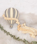 Wooden Hot Air Balloon Monthly Milestone Cards For Babies on a fluffy surface with leaves, featuring a striped balloon design.