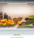 Under-cabinet lighting illuminating kitchen counter with fruits and vegetables, showcasing 18 Inch Dimmable Under Cabinet Lighting With Swivel Lens 3CCT 2700K to 4000K Plug In Or Hardwired 50 Degree Rotatable Lens And 110 Degree Beam Linkable Kitchen LED Bar Light White ETL.