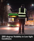 Heavy Duty Reflective Mesh Safety Vest For Men In Black With Nine Roomy Pockets And Bright High Visibility Markers For Construction Job Sites Serving Up Top Tier Airflow And Zero Hassle Comfort worn by a worker directing traffic at night.