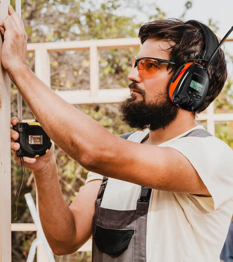 Worker wearing Bluetooth Hearing Protection Headphones With AM FM Radio 25dB NRR Rechargeable, measuring wood on site.