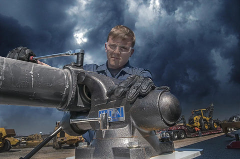 Beefy Pro Grade Tradesman XC Bench Vise With Six And A Half Inch Jaw Width, Six Inch Opening, Four Inch Throat, 360 Degree Swivel Base With Double Lockdowns, 60,000 PSI Ductile Iron Body For Lifetime Smooth Operation, Enclosed Design Keeps Lubrication. Worker using heavy-duty bench vise outdoors