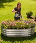 Person watering plants in a Galvanized Raised Garden Bed Kit 4By2By1Ft Oval Planter Boxes For Outdoor Garden on grass