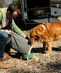 Man using Dog Food Travel Bag Large Capacity For RV Trips And Camping Collapsible Kibble Carrier With Roll Down Top 21 Cups Grey to feed dog outdoors.