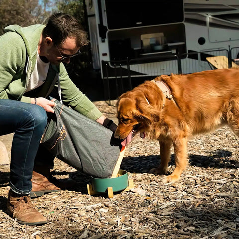 Man using Dog Food Travel Bag Large Capacity For RV Trips And Camping Collapsible Kibble Carrier With Roll Down Top 21 Cups Grey to feed dog outdoors.