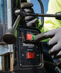 Makita HB350 magnetic drill front view; black control panel with red on/off switch and gloved hand.