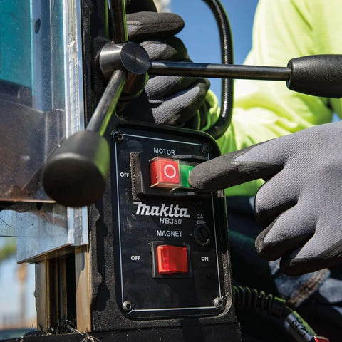 Makita HB350 magnetic drill front view; black control panel with red on/off switch and gloved hand.