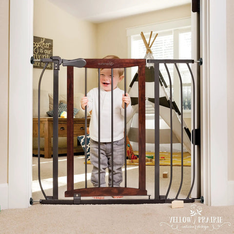 Walk Through Baby And Pet Gate With Walnut Wood And Charcoal Metal Accents installed in doorway with child standing behind