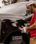 Man cleaning hands with Heavy Duty Cleaning Wipes For Paint Prep And Degreasing by a truck. Flat pack visible on tire.