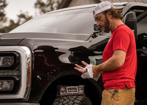 Man cleaning hands with Heavy Duty Cleaning Wipes For Paint Prep And Degreasing by a truck. Flat pack visible on tire.