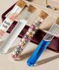 Four clear 10ml plastic test tubes with corks filled with bath salts, beads, and liquid from the All In One 21 Piece Plastic Test Tubes Kit With Corks And Stand 10Ml Tubes For Bath Salts Party Favors DIY Crafts And Spice Storage Shatterproof Leak Proof Reusable Clear And Easy To Organize Rack.