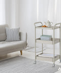 Front view of a beige three-tier rolling cart with swivel caster wheels and handles; AXL logo visible.