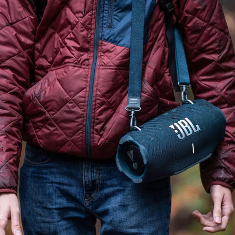 Person wearing a maroon jacket carrying Xtreme 4 Portable Bluetooth Speaker Delivers Beast Mode Sound With Deep Bass, IP67 Waterproof Durability.