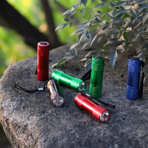 Assorted colored 20-Pack Aluminum 6-LED Flashlights Set with Lanyard, AAA Batteries Included, placed on a rock outdoors