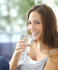 Woman smiling while holding a glass of water, enjoying hydration at home with Replacement Alkaline Filter For 109 Water Pitcher 2 Pack